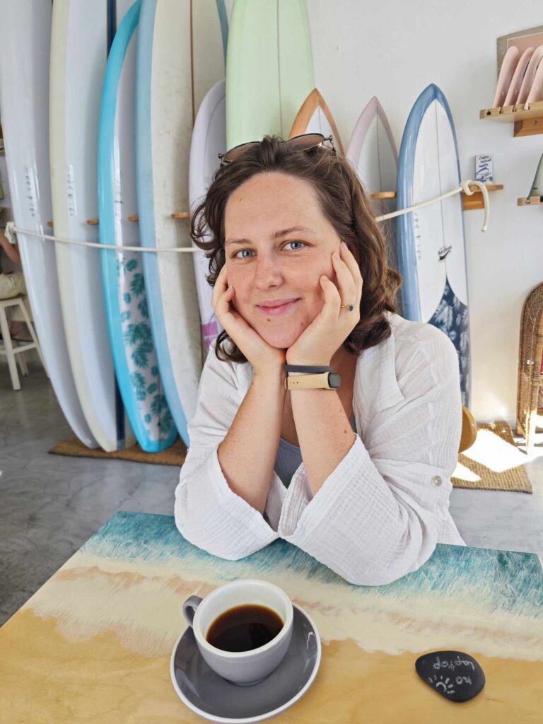 Kobieta z filiżanką kawy i deskami surfingowymi w tle